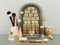 Adventskalender Frauen Kosmetik: Pinsel, Parfum und Lippenstift warten hinter den Türchen. Goldene Kugeln und Weihnachtsbäume schmücken die Szene.