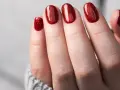 Glitzernde rote Gel-Nagel-Designs auf einer Hand, die aus einem grauen Pullover ragt.