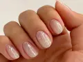 Nahaufnahme einer Hand mit ovalen Nägeln, die mit schimmerndem Glitzer-Nagellack in Pastelltönen verziert sind.