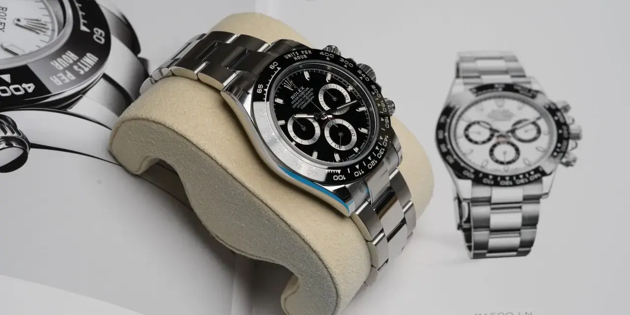 Luxuriöse Rolex Daytona Uhr auf einem Kissen vor einem Buch mit Uhrenabbildungen.