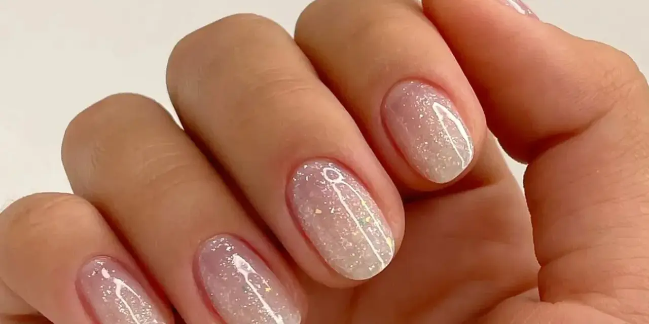 Nahaufnahme einer Hand mit ovalen Nägeln, die mit schimmerndem Glitzer-Nagellack in Pastelltönen verziert sind.