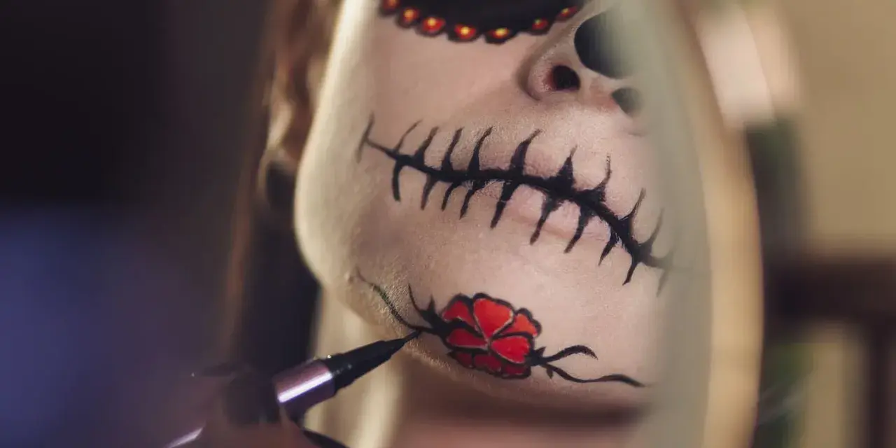 Nahaufnahme eines Gesichts mit Totenkopf-Make-up, das mit einem Pinsel bemalt wird.
