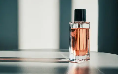 Eine Glasflasche mit rosafarbenem Parfum und schwarzem Deckel, beleuchtet von Sonnenlicht.