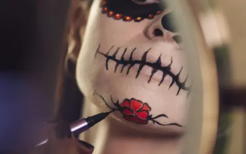 Nahaufnahme eines Gesichts mit Totenkopf-Make-up, das mit einem Pinsel bemalt wird.