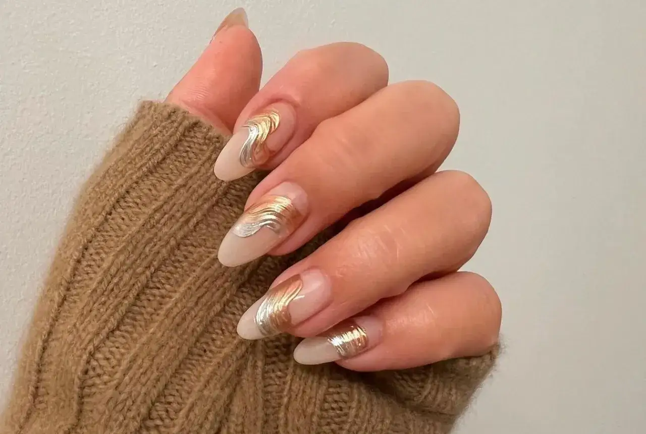 Elegantes gel nagel design mit wellenförmigen Gold- und Silberakzenten auf nudefarbenem Untergrund.
