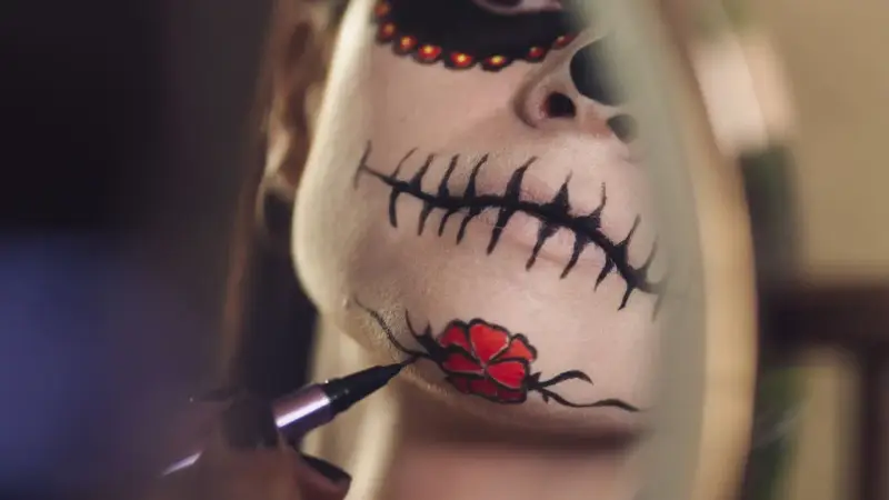 Nahaufnahme eines Gesichts mit Totenkopf-Make-up, das mit einem Pinsel bemalt wird.